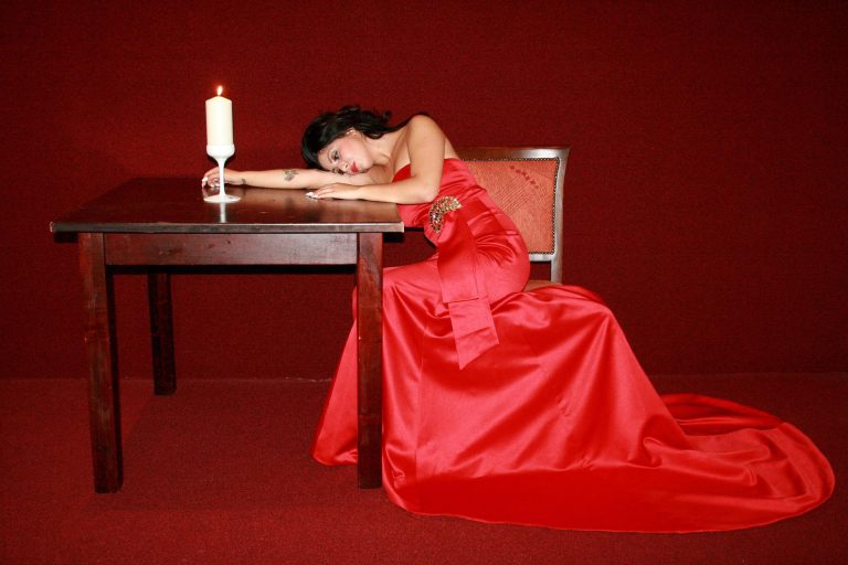 sad woman in a red gown hunching on a table next to a candle